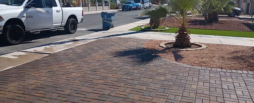 A finished interlocking paver driveway in Las Vegas, with a palm set into a decorative rock bed and a strip of synthetic turf alongside.