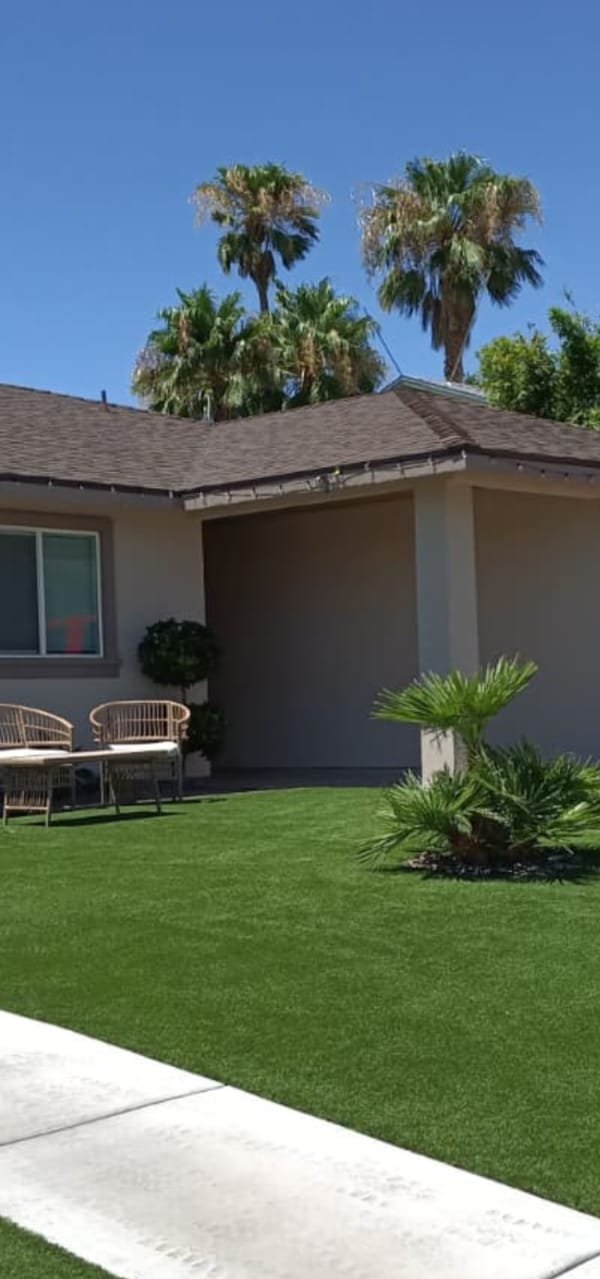 A front yard laid with synthetic turf, edged against a clean concrete walkway.